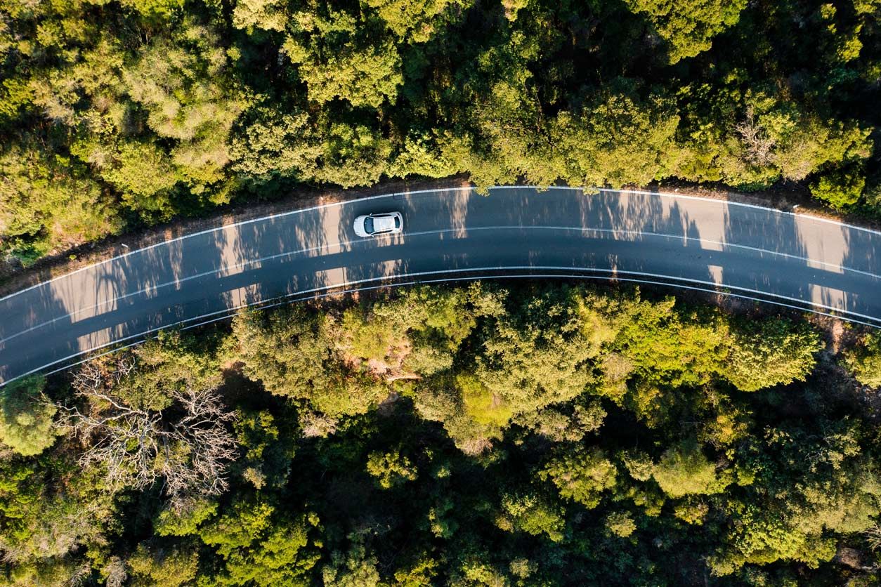 Vogelperspektive auf eine Straße auf der ein Auto fährt. Umrandet wird die Straße von Wald.
