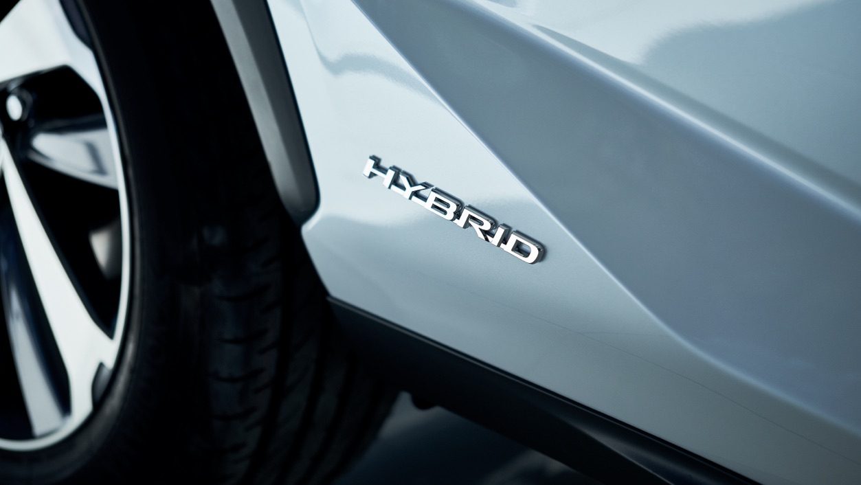 Detailaufnahme der Seitenwand eines silbernen Hybridautos. Auf dem Blech steht das Wort "HYBRID". Ein Teil des rechten Hinterrads ist zu sehen.