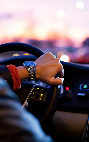 Mann fährt im Auto dem Sonnenuntergang entgegen. Nahaufnahme des Lenkrads und des Armes,