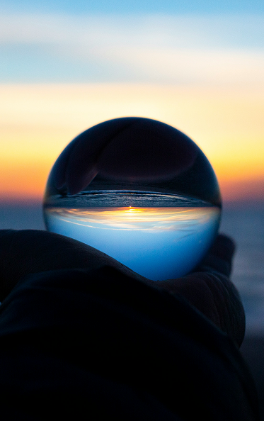 Sonnenuntergang im Hintergrund, Kugel als Zeichen für die Zukunft im Vordergrund, gehalten von einer Hand.