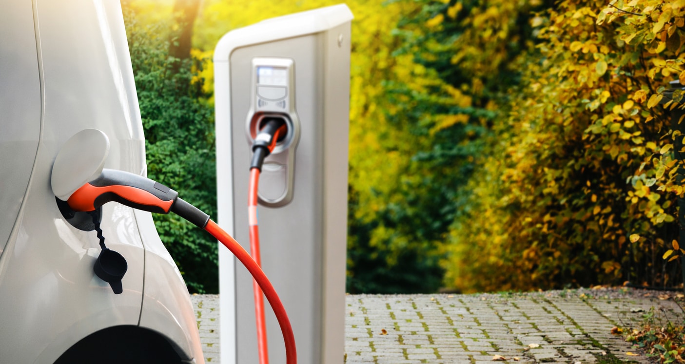 Elektroauto wird geladen. Im Hintergrund sieht man ein Dach mit PV-Anlage.