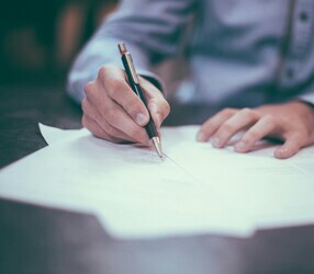 Une main masculine tient un stylo et signe des documents.