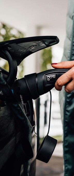 Une main tient la prise d'une voiture électrique en charge.