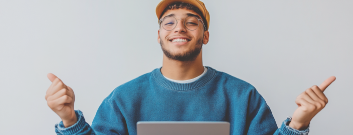 Jeune homme souriant, vêtu d'un pull bleu et d'une casquette brune, assis devant son ordinateur portable et montrant ses deux pouces. Il se réjouit des prestations incluses dans son abonnement véhicule électrique.