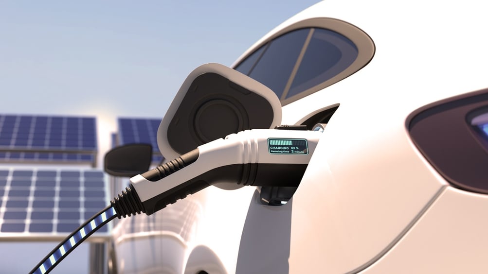 Voiture électrique en cours de recharge. En arrière-plan, on peut voir un toit équipé d'une installation photovoltaïque (PV).