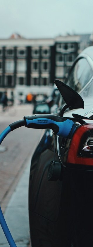 L'immagine mostra un'auto elettrica nera collegata alla presa di corrente in una città.