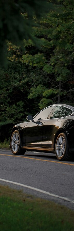 Un'auto elettrica nera sta viaggiando su una strada fiancheggiata da alberi.