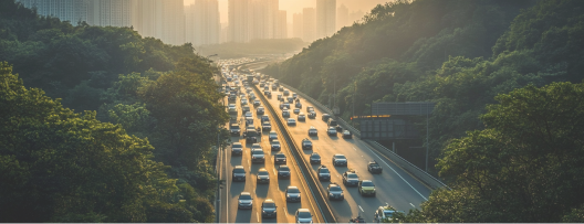 Veduta aerea di un'autostrada trafficata circondata da boschi. All'orizzonte si vede una grande città.
