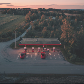 Twee rode elektrische auto's staan geparkeerd bij een snellaadstation op het platteland. De zon gaat onder.