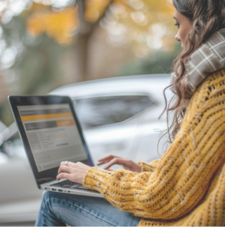Een vrouw in een gele trui leest op haar laptop informatie voor over verzekeringskosten en -voordelen voor haar elektrische auto. 
