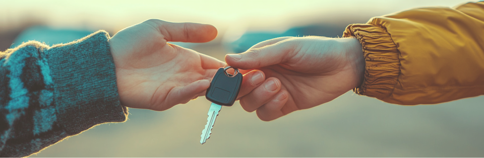 Close-up van twee handen. De rechterhand overhandigt een autosleutel aan de linkerhand na de verkoop van de elektrische auto.